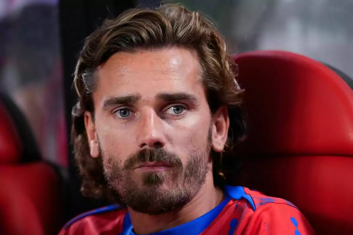 Hombre con barba y cabello largo sentado en un asiento rojo.