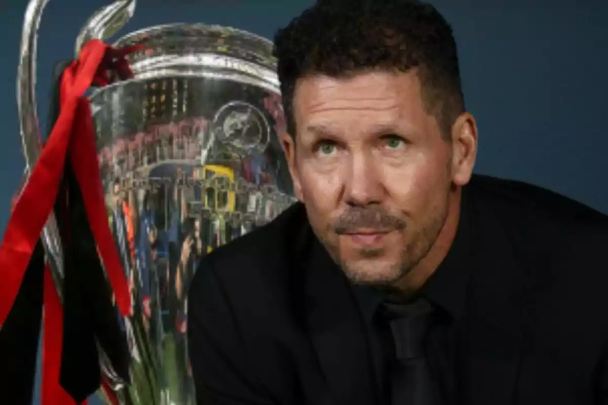 A man in a dark suit next to a large silver trophy with red and black ribbons.