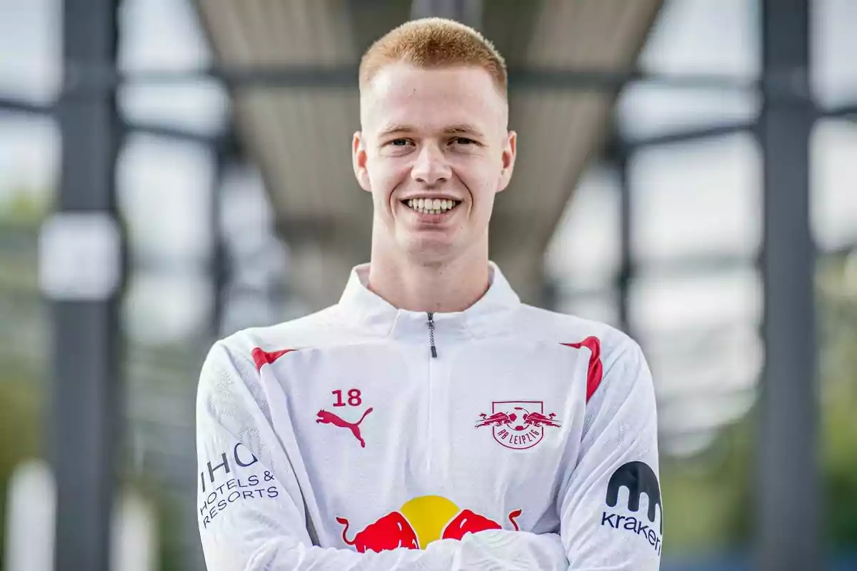 Un joven con el uniforme del equipo de fútbol RB Leipzig sonríe con los brazos cruzados.