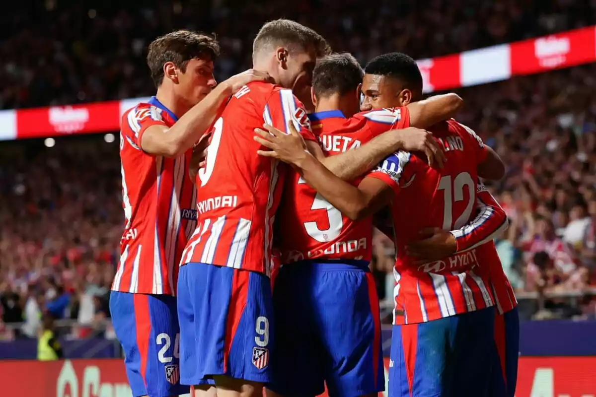 Jugadores de fútbol con uniformes rojos y blancos celebrando en el campo.