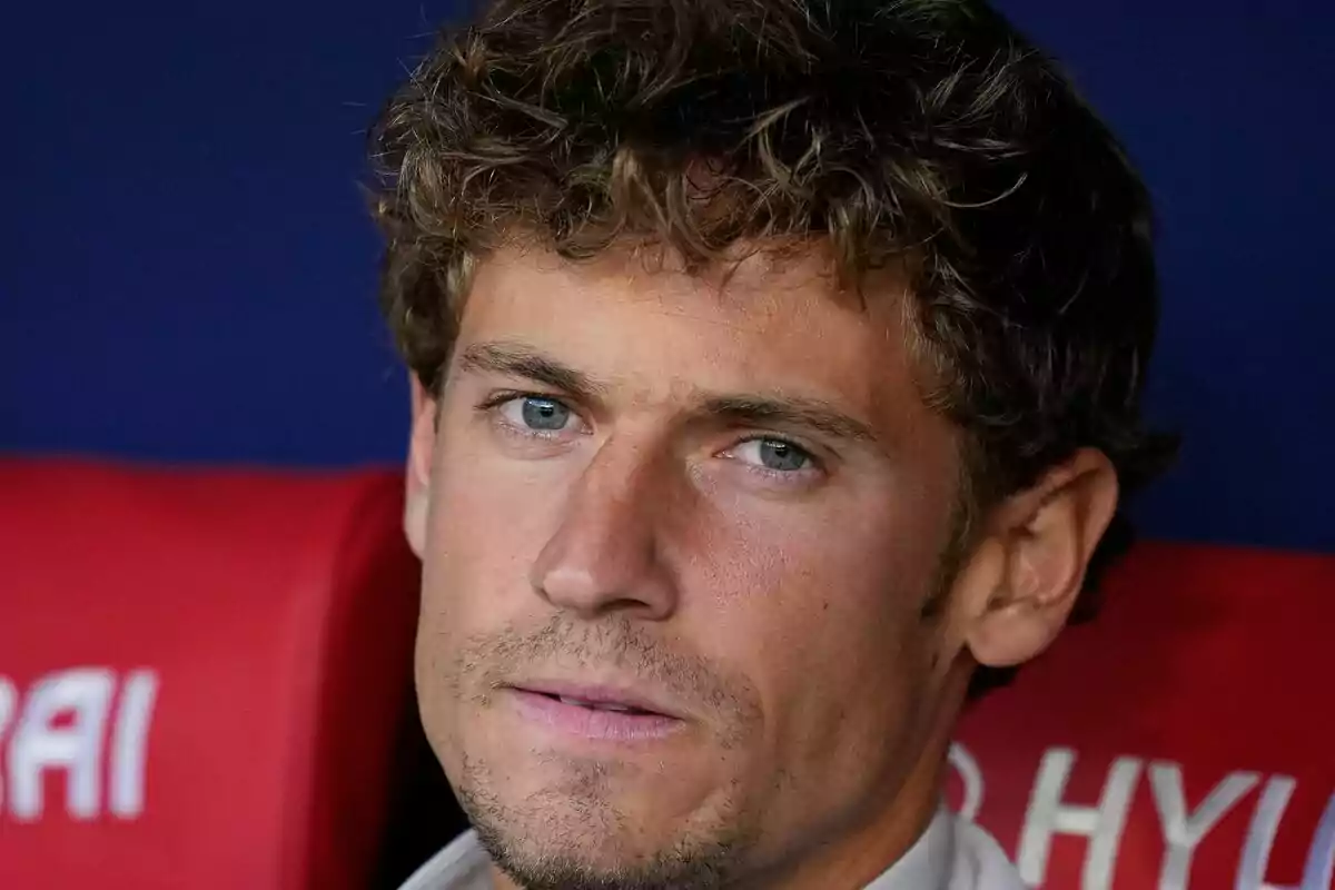 A curly-haired man with light-colored eyes sitting in a red seat.