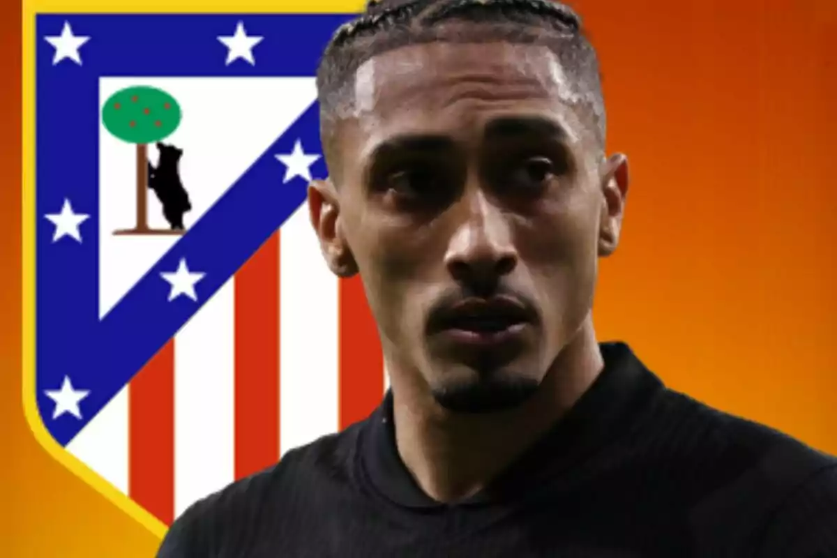 Futbolista con camiseta negra frente al escudo del Atlético de Madrid sobre un fondo naranja