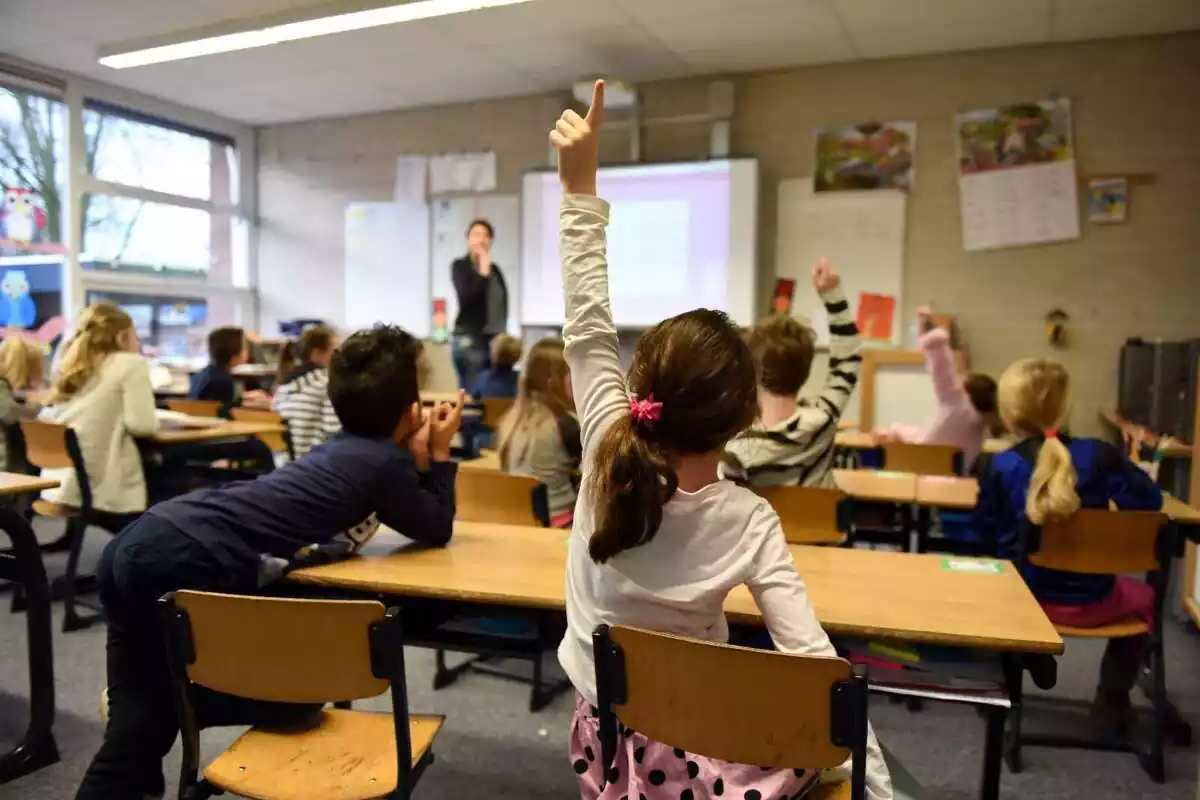 Aula de un colegio con alumnos de primaria levantando el brazo Aula de un colegio con alumnos de primaria levantando el brazo