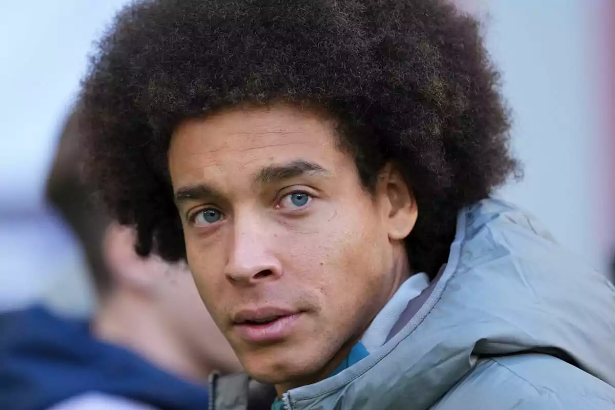 A man with curly hair and a gray jacket looking at the camera.