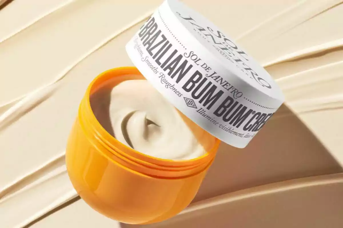 Envase amarillo de crema corporal Brazilian Bum Bum Cream de Sol de Janeiro abierto mostrando la textura cremosa del producto sobre un fondo beige Envase amarillo de crema corporal Brazilian Bum Bum Cream de Sol de Janeiro abierto mostrando la textura cremosa del producto sobre un fondo beige