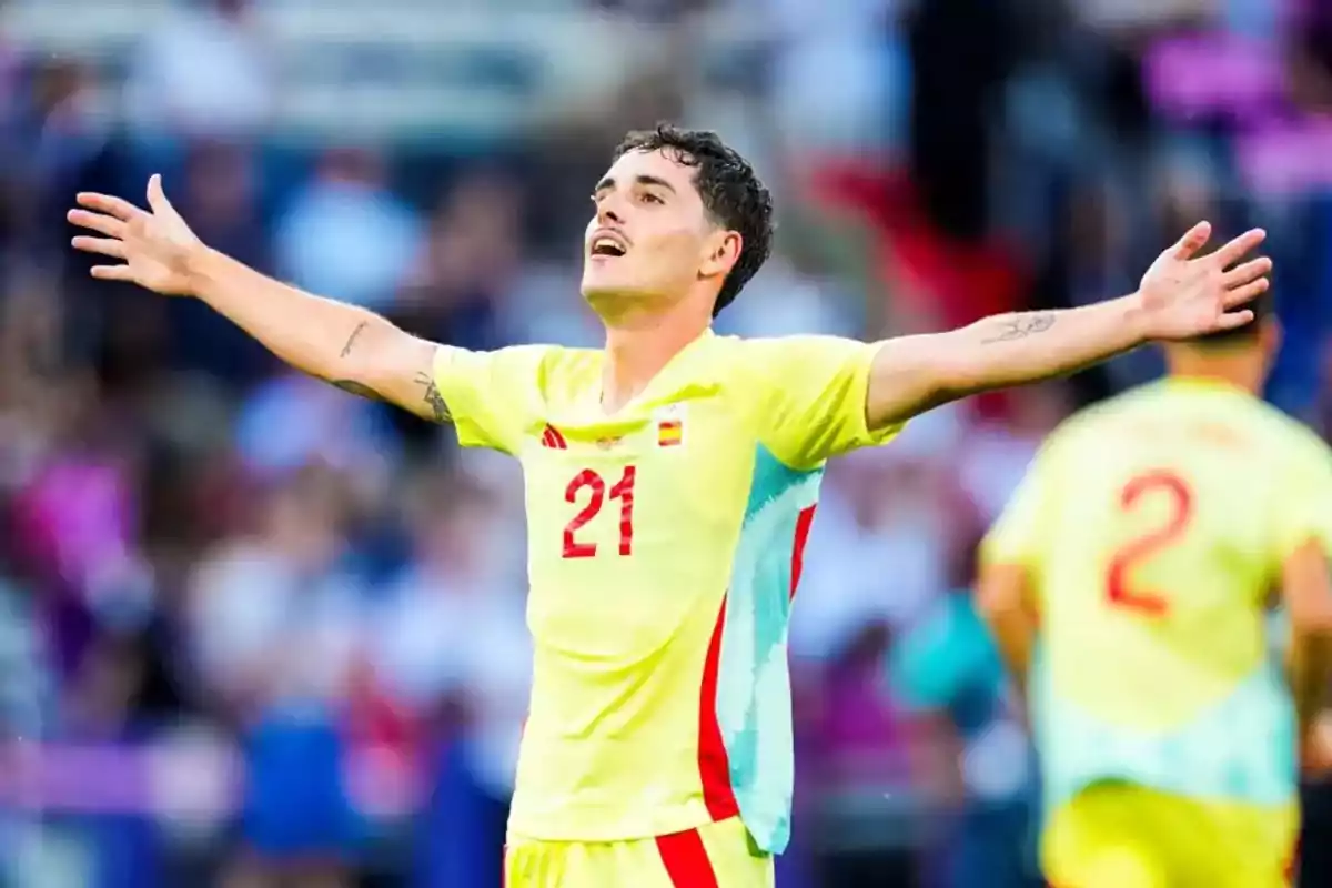 Football player in the yellow uniform of the Spanish national team celebrating with his arms outstretched in a stadium. Football player in the yellow uniform of the Spanish national team celebrating with his arms outstretched in a stadium.