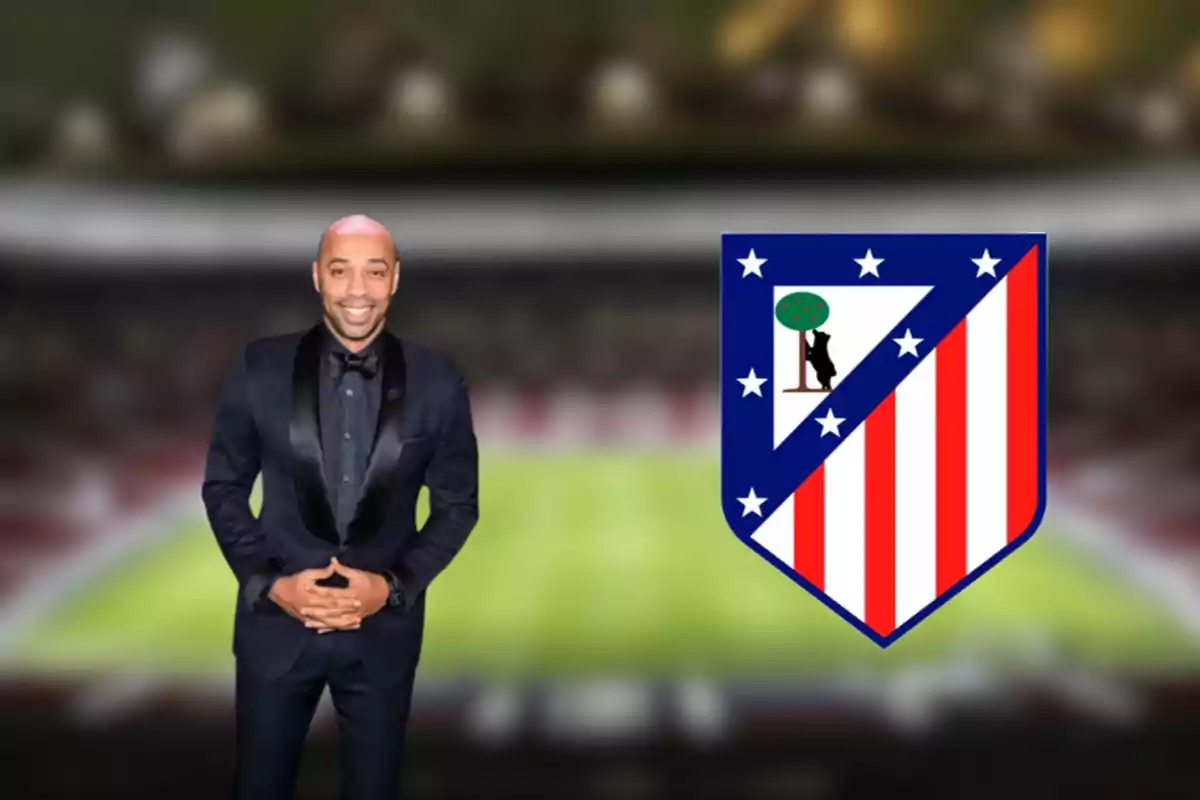 Un hombre con traje oscuro sonríe frente a un estadio de fútbol, junto al escudo del Atlético de Madrid.