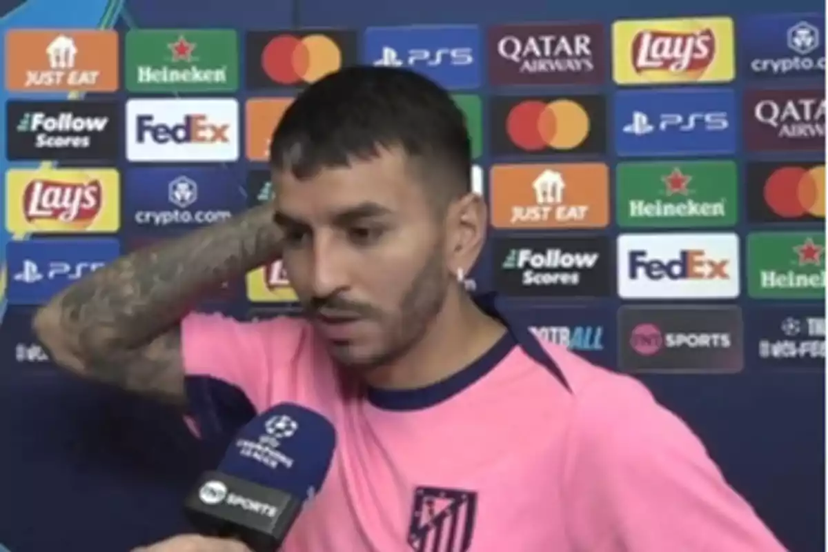 Un jugador de fútbol con camiseta rosa del Atlético de Madrid siendo entrevistado frente a un panel de patrocinadores.