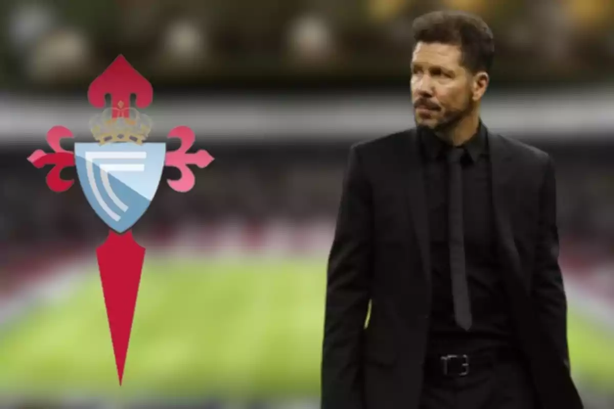 Un hombre con traje negro de pie junto al escudo del Celta de Vigo en un estadio de fútbol.