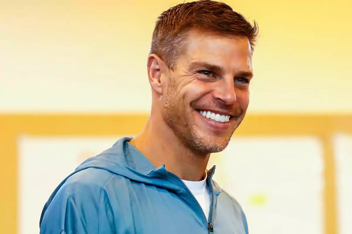 Un hombre sonriente con chaqueta azul en un fondo amarillo.