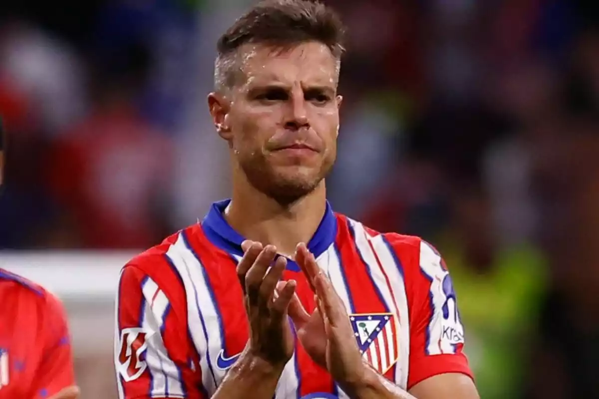 Jugador de fútbol con uniforme del Atlético de Madrid aplaudiendo en el campo.