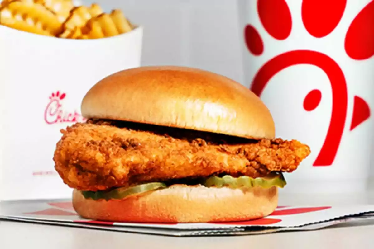 Sándwich de pollo empanizado con pepinillos acompañado de papas fritas y un vaso de bebida