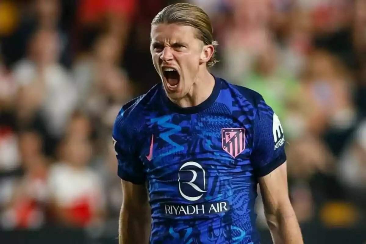 Un jugador de fútbol con una camiseta azul y rosa grita con emoción durante un partido.