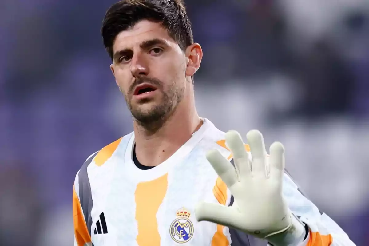 Un futbolista con uniforme de portero del Real Madrid levanta la mano con un guante blanco.