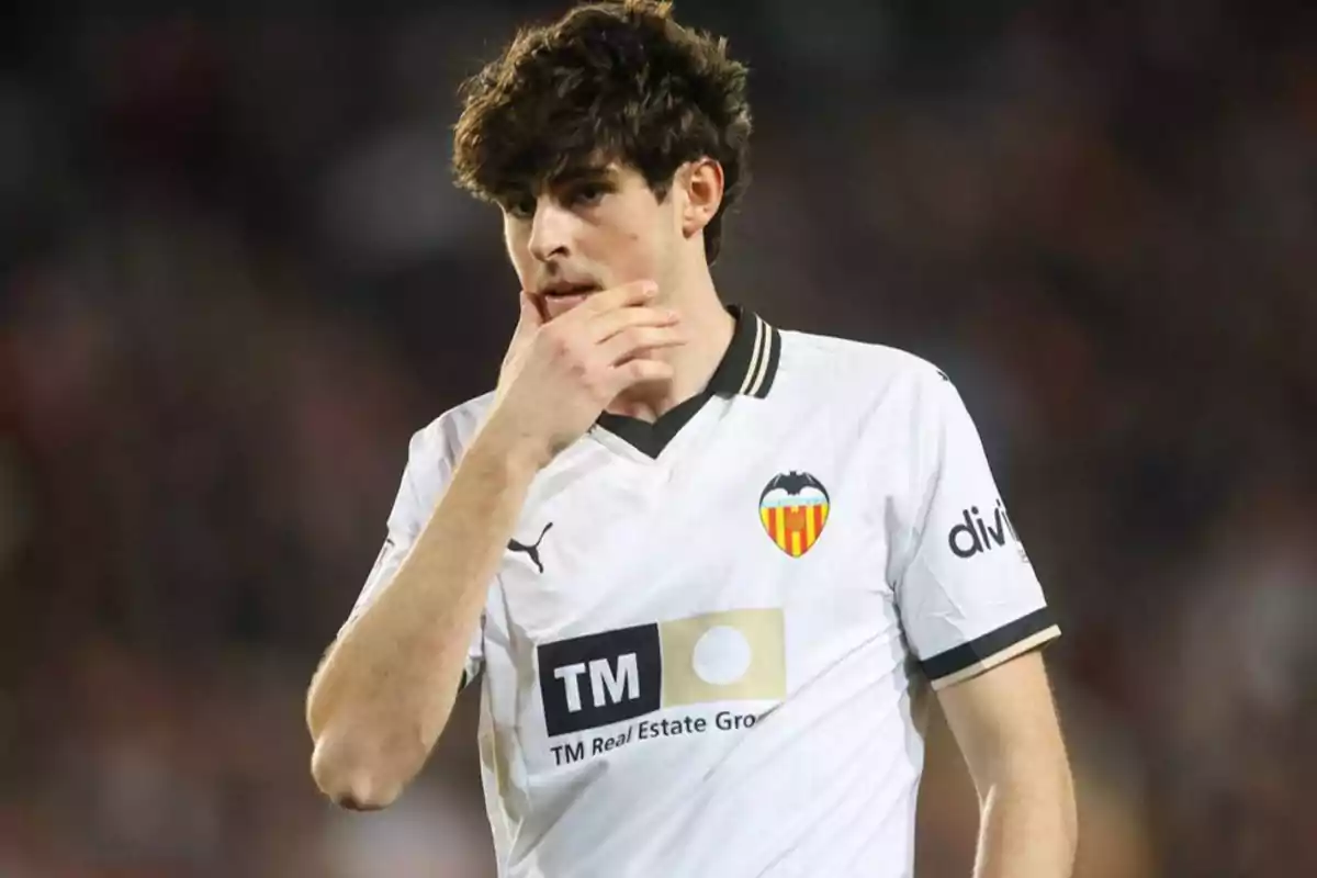 Un jugador de fútbol con la camiseta del Valencia CF se lleva la mano al rostro durante un partido.