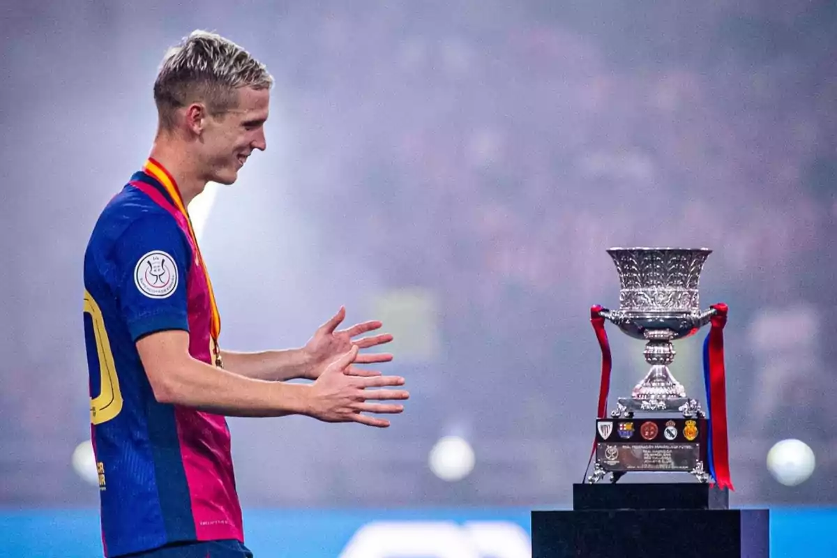 Un jugador de fútbol con una medalla observa un trofeo en un estadio.