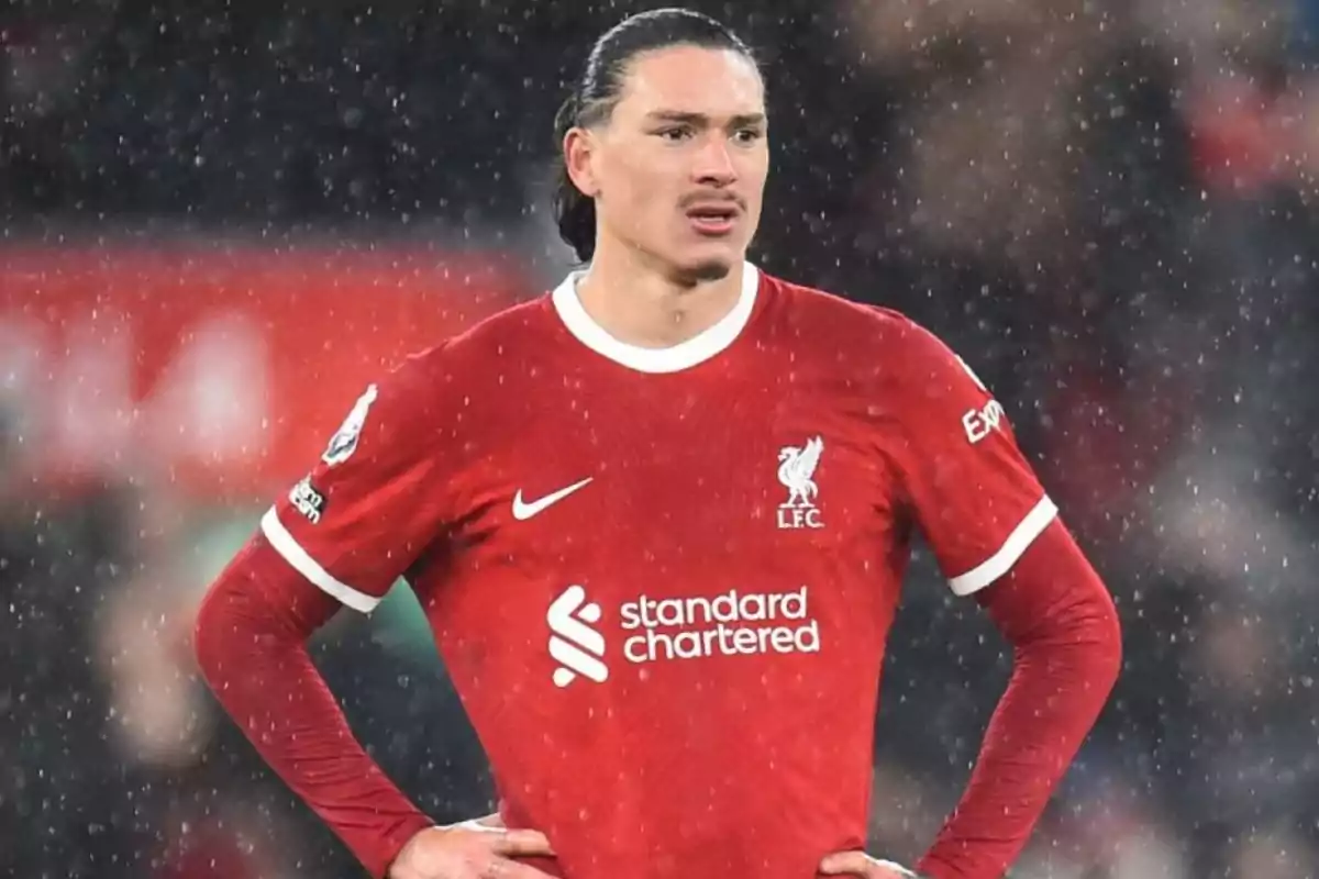 Un jugador de fútbol con el uniforme rojo del Liverpool FC está de pie bajo la lluvia en el campo.