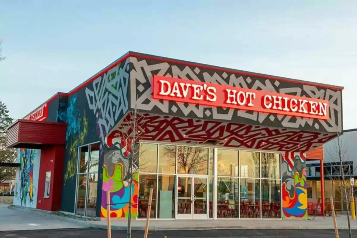 Restaurante Dave's Hot Chicken con fachada decorada con arte urbano y letrero luminoso rojo Restaurante Dave's Hot Chicken con fachada decorada con arte urbano y letrero luminoso rojo