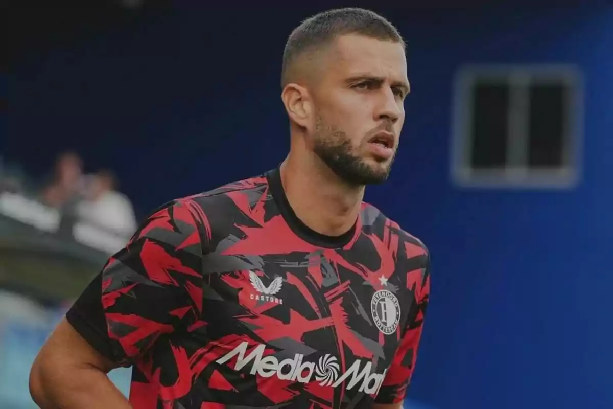 Un jugador de fútbol con una camiseta de entrenamiento roja y negra con el logo de "MediaMarkt" y "Castore" en el pecho.