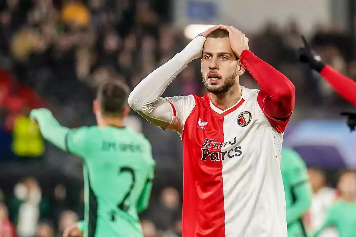 Un jugador de fútbol con uniforme rojo y blanco se lleva las manos a la cabeza en un gesto de frustración durante un partido.