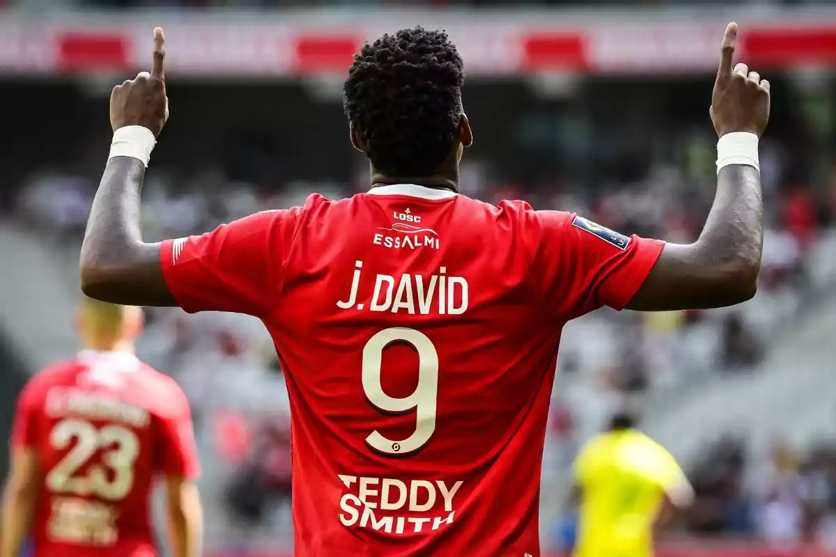 Jugador de fútbol con la camiseta roja número 9 levantando los brazos en un estadio.