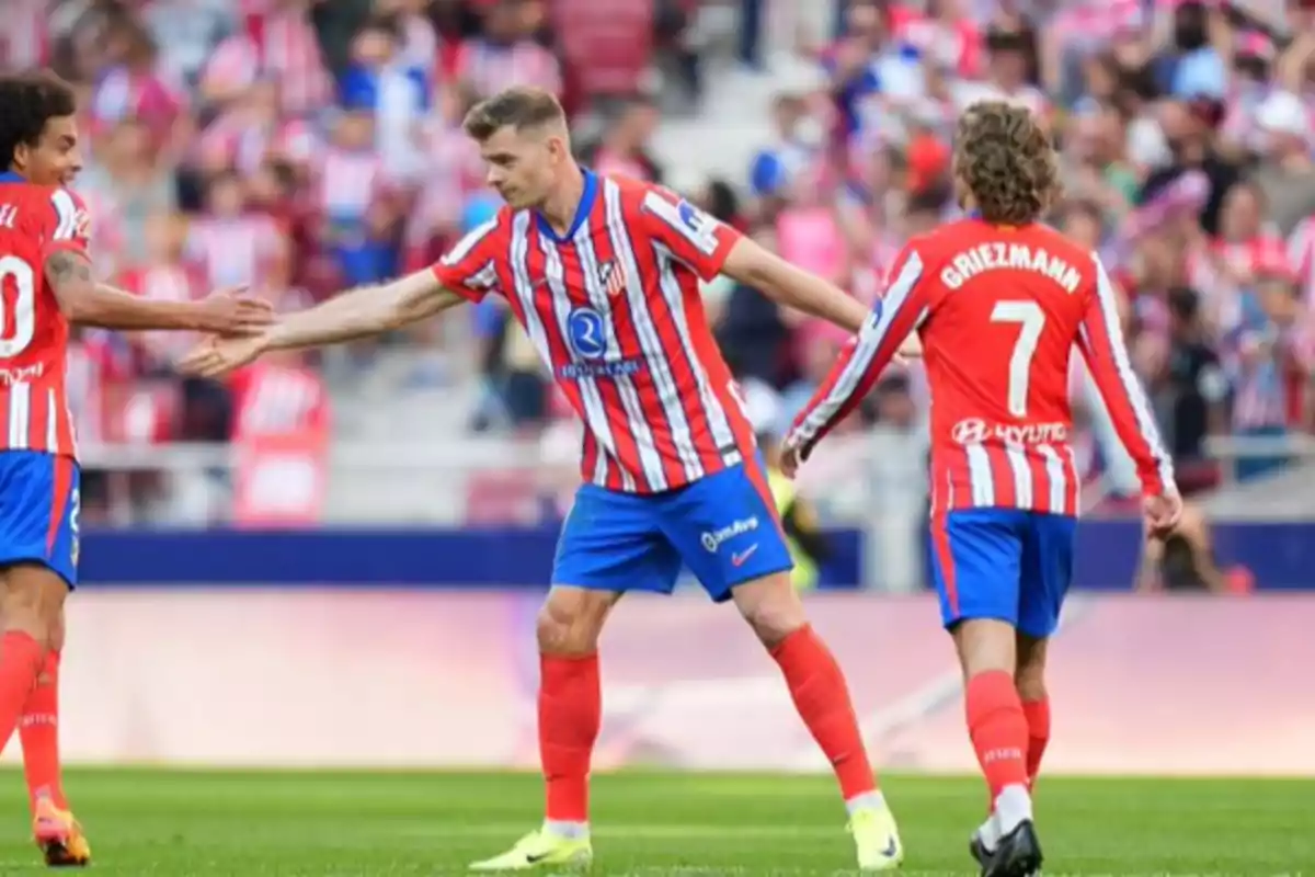 Jugadores de fútbol del Atlético de Madrid celebrando en el campo con uniformes rojos y blancos.