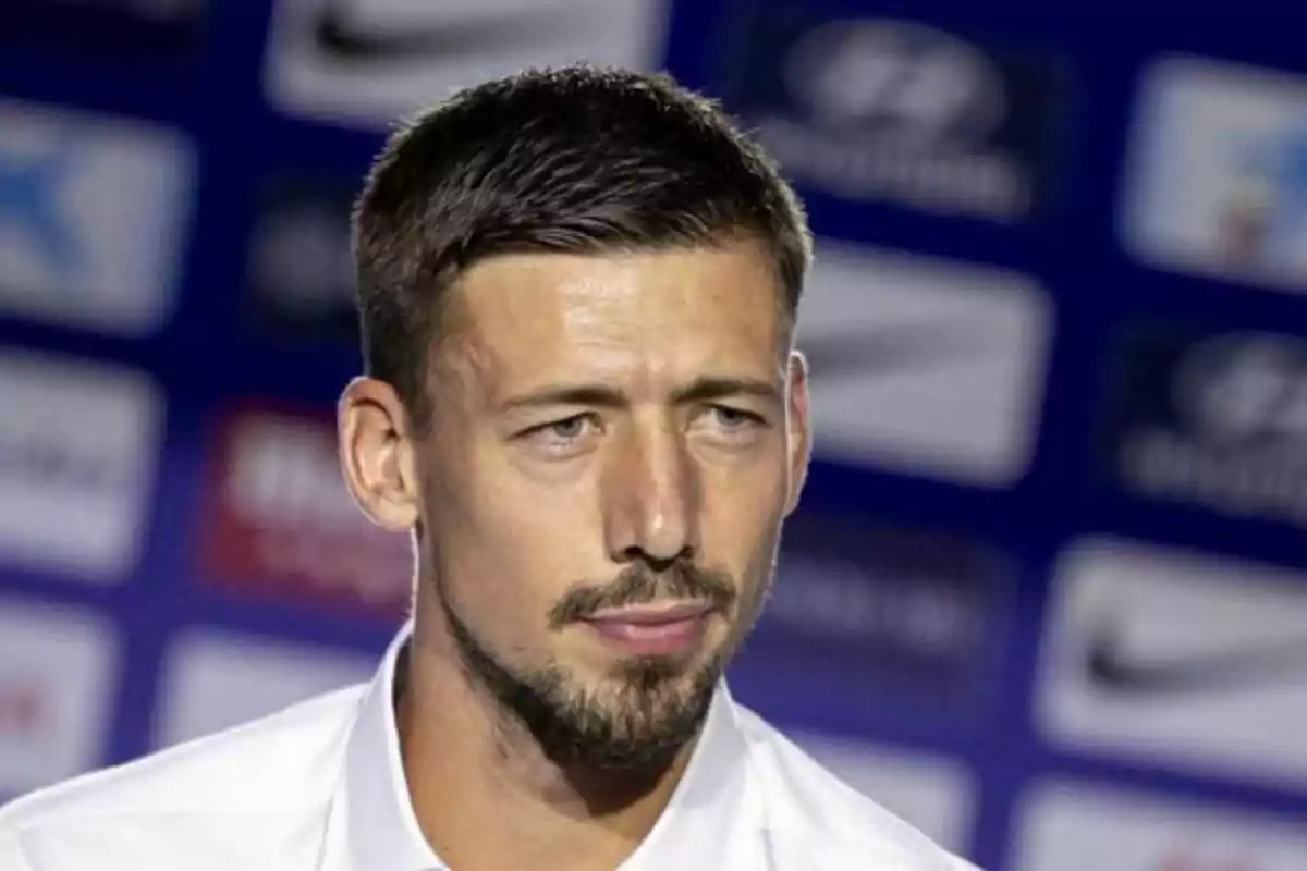 Hombre con barba y cabello corto en una conferencia de prensa con fondo borroso de logotipos.