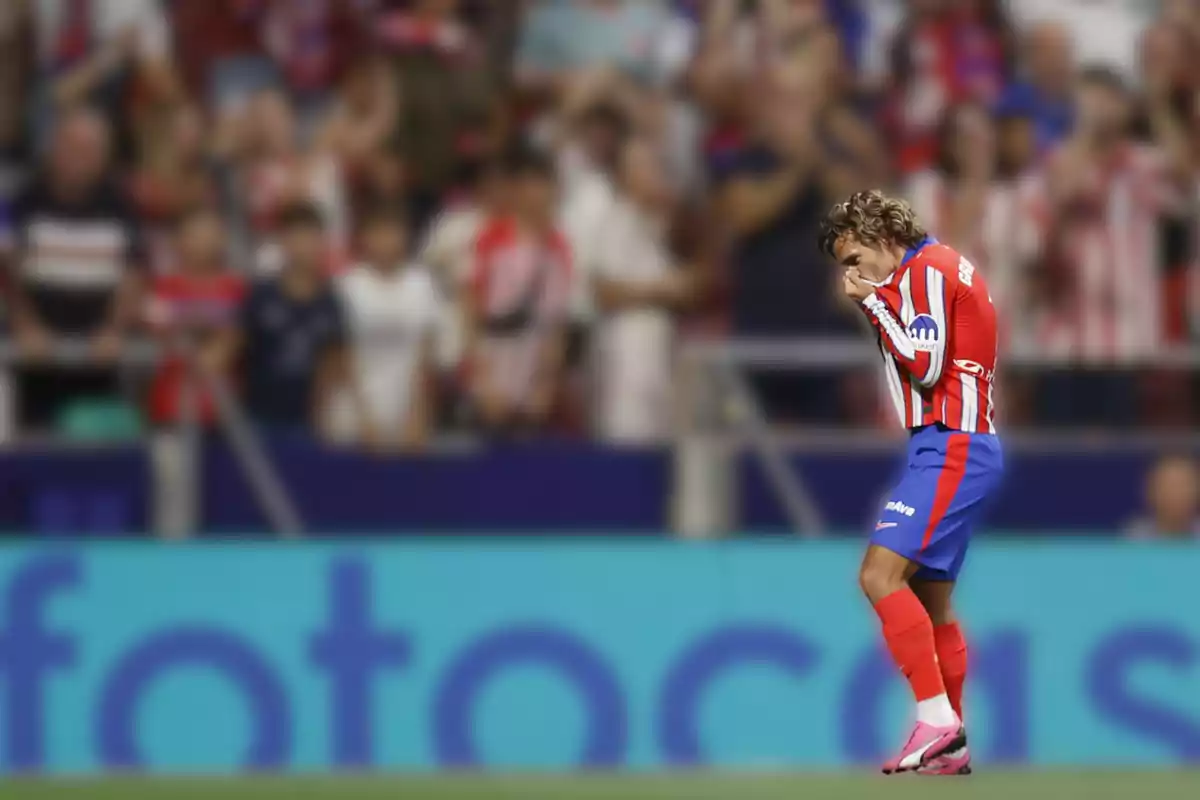 Un jugador de fútbol con uniforme rojo y blanco besa su camiseta en el campo mientras el público en las gradas observa.