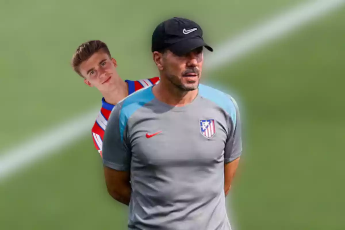 Dos hombres con ropa deportiva del Atlético de Madrid, uno con camiseta de rayas rojas y blancas y el otro con camiseta gris y gorra negra, sobre un fondo de campo de fútbol.