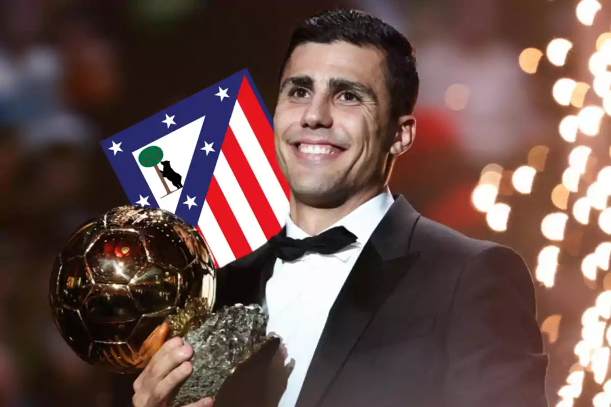 Un hombre sonriente en traje sostiene un trofeo dorado con un fondo de luces brillantes y el escudo del Atlético de Madrid.