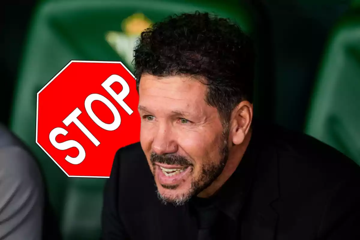 Un hombre con barba y cabello rizado está sonriendo con un cartel de stop rojo al fondo.