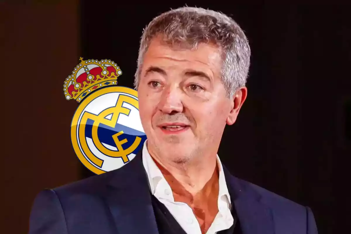 A grey-haired man in a dark suit and white jersey stands in front of a dark background with the Real Madrid crest behind him.