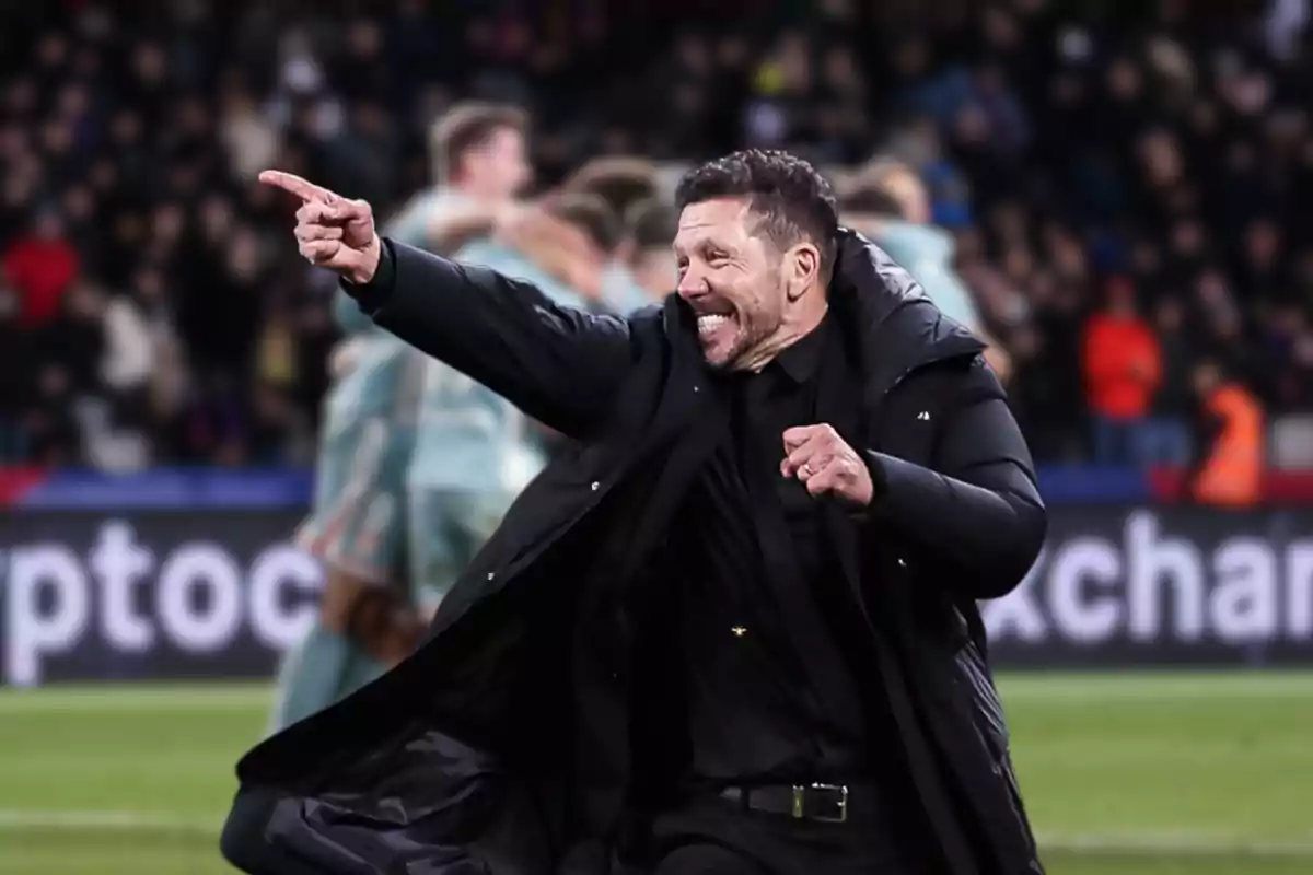 Un hombre con abrigo negro celebra en un estadio lleno de espectadores.