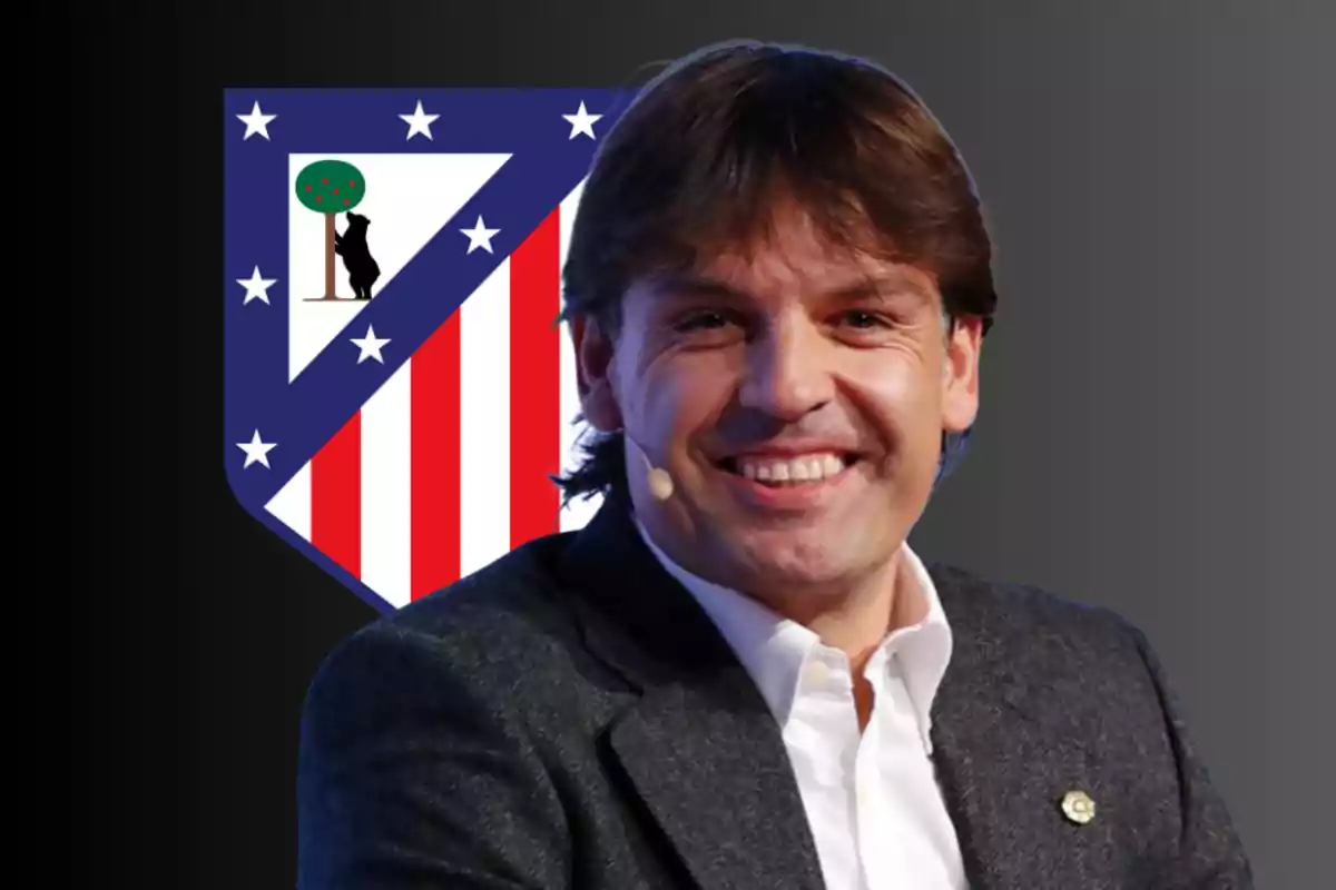 Un hombre sonriente con un micrófono en la oreja frente al escudo del Atlético de Madrid.