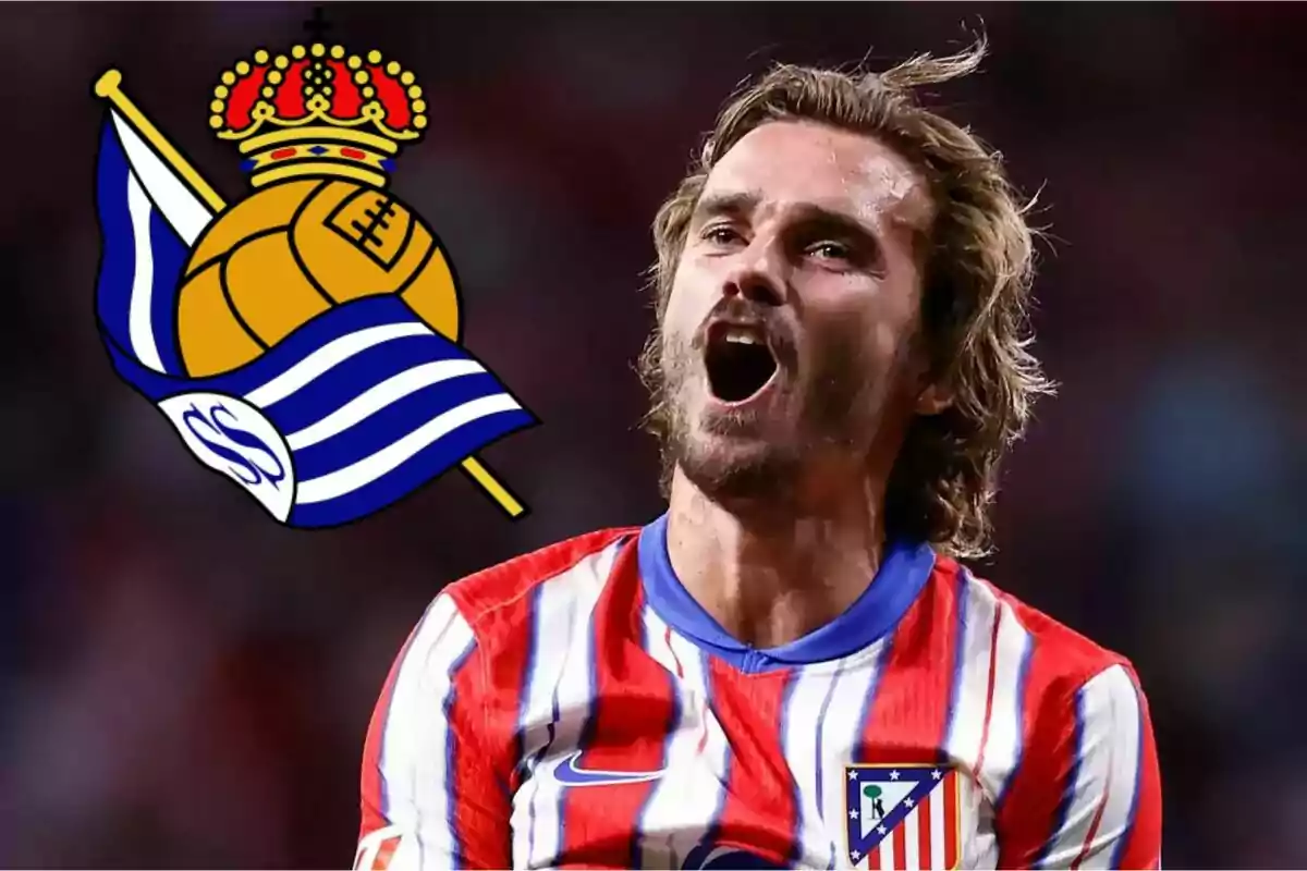 Un jugador de fútbol con la camiseta del Atlético de Madrid celebra con el escudo de la Real Sociedad al fondo.