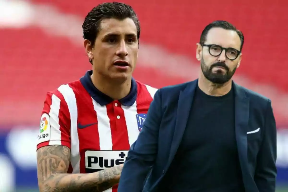 Un jugador de fútbol con el uniforme del Atlético de Madrid y un hombre con gafas y barba vestido con un traje oscuro están en un estadio con fondo rojo.