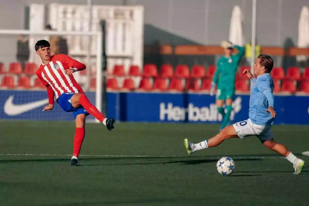 Two soccer players compete for the ball in a game, one wearing a red and white uniform and the other wearing a light blue uniform.