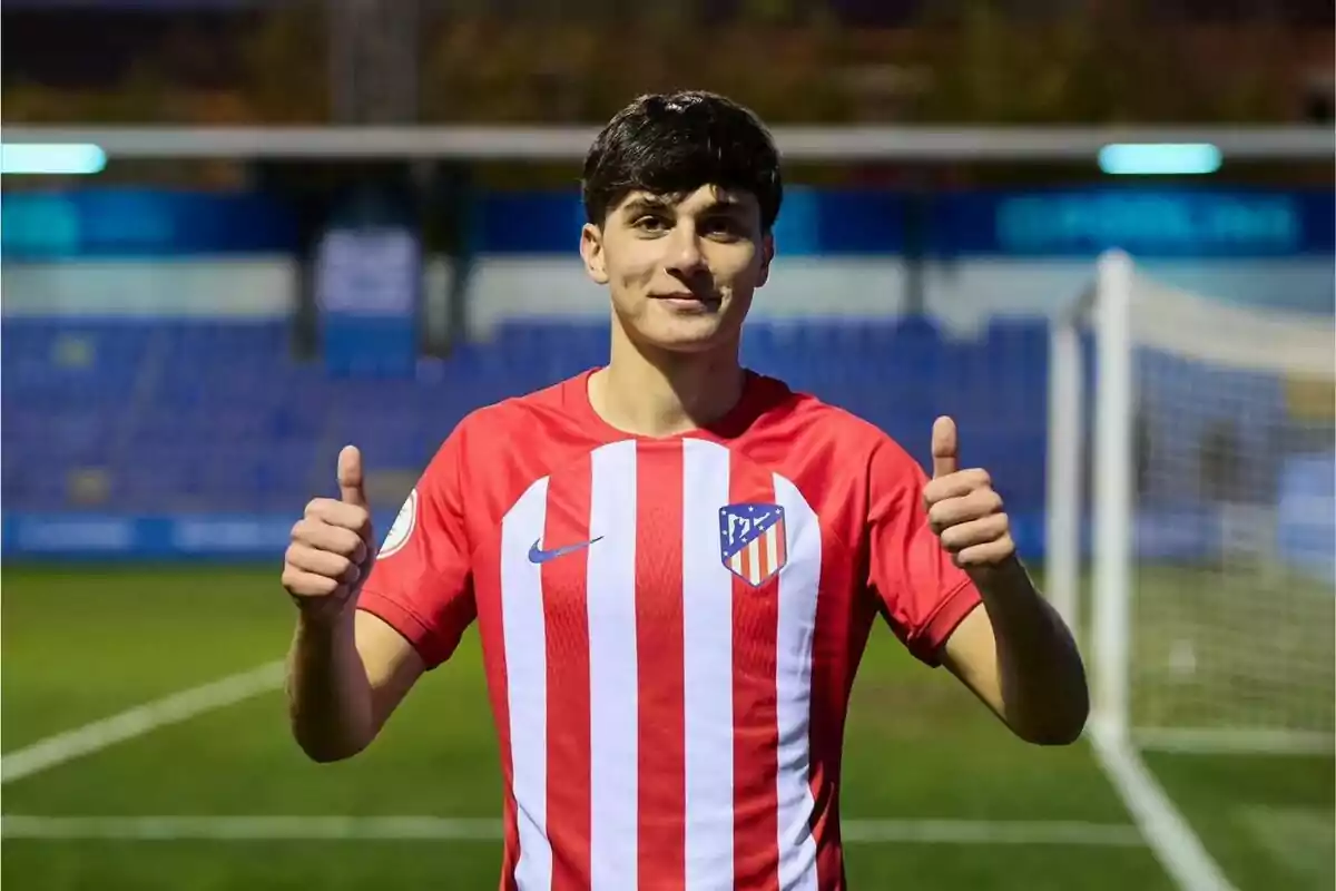 A football player wearing an Atlético de Madrid shirt giving both thumbs up on a football pitch.