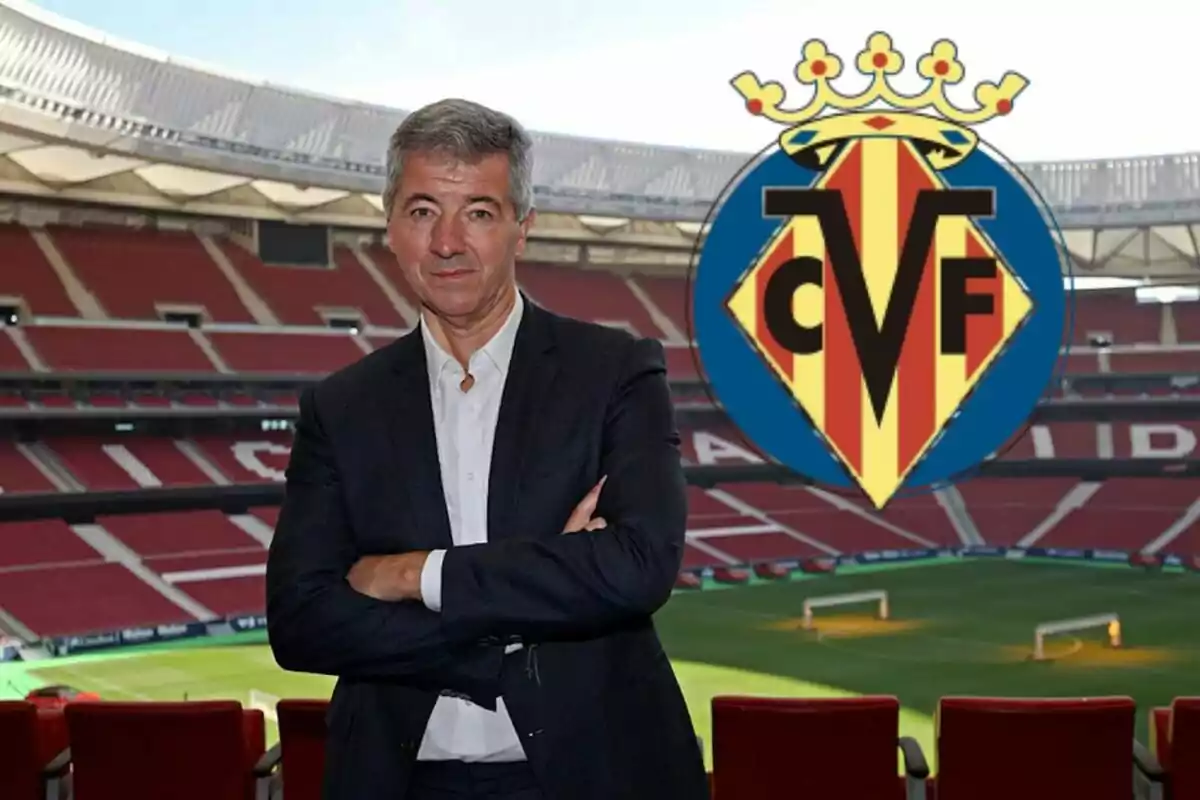 Hombre de traje posando en un estadio de fútbol con el escudo del Villarreal CF al fondo.