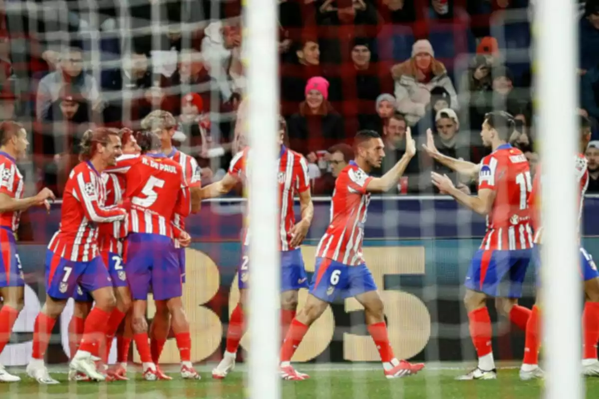 Jugadores de fútbol con uniforme rojo y blanco celebran en el campo mientras el público observa desde las gradas.