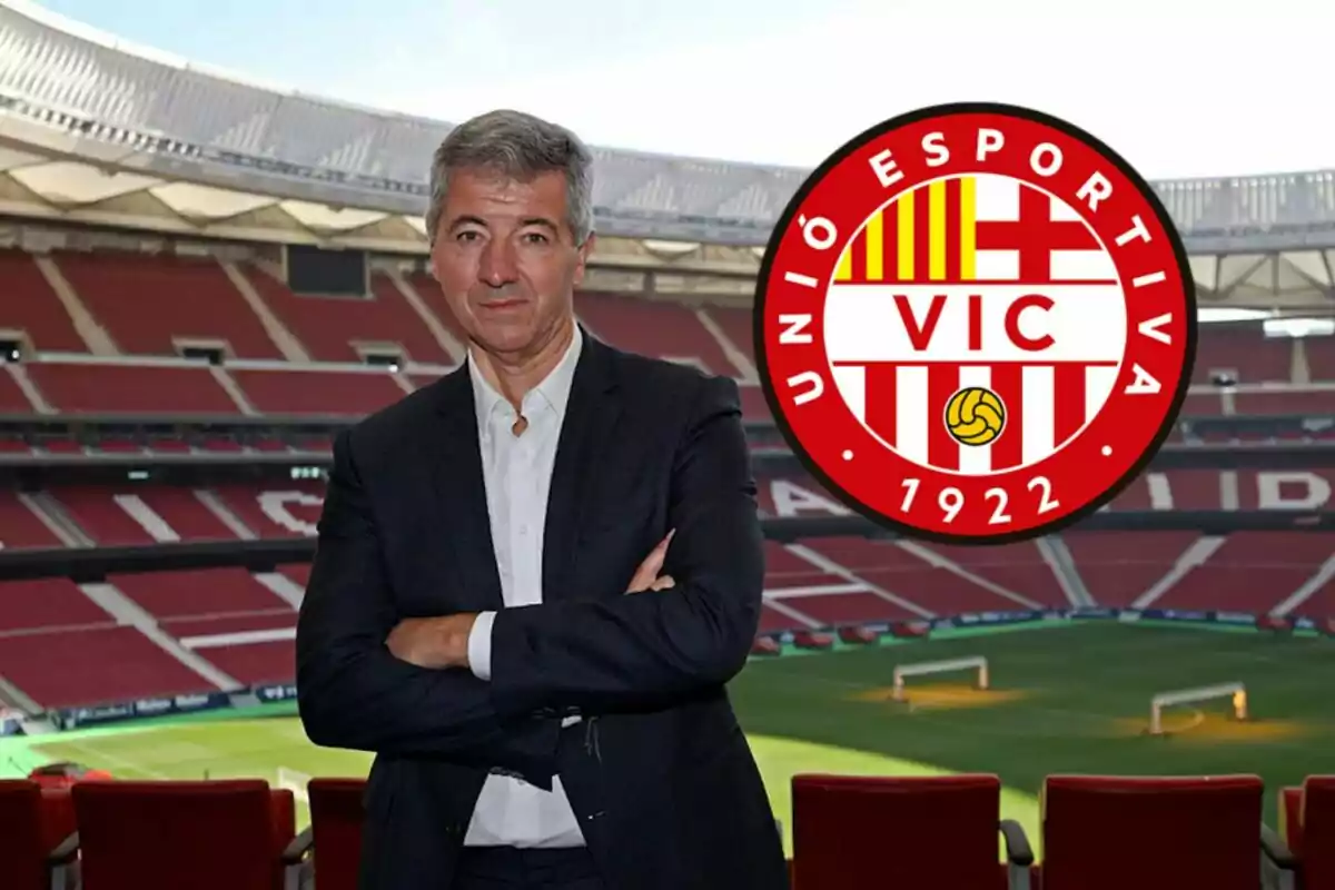 Hombre de traje posando en un estadio de fútbol con el escudo de Unió Esportiva Vic al lado.