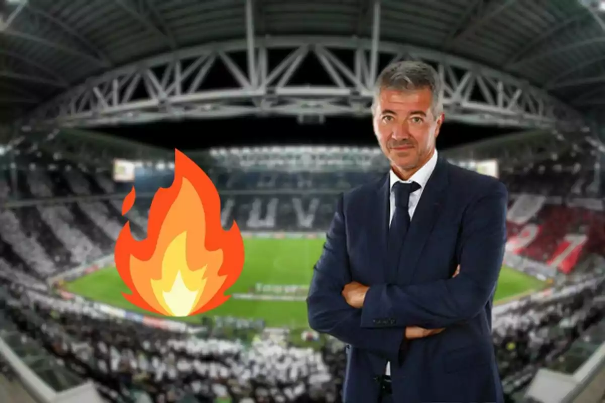 Un hombre de traje con los brazos cruzados en un estadio de fútbol con un emoji de fuego superpuesto.