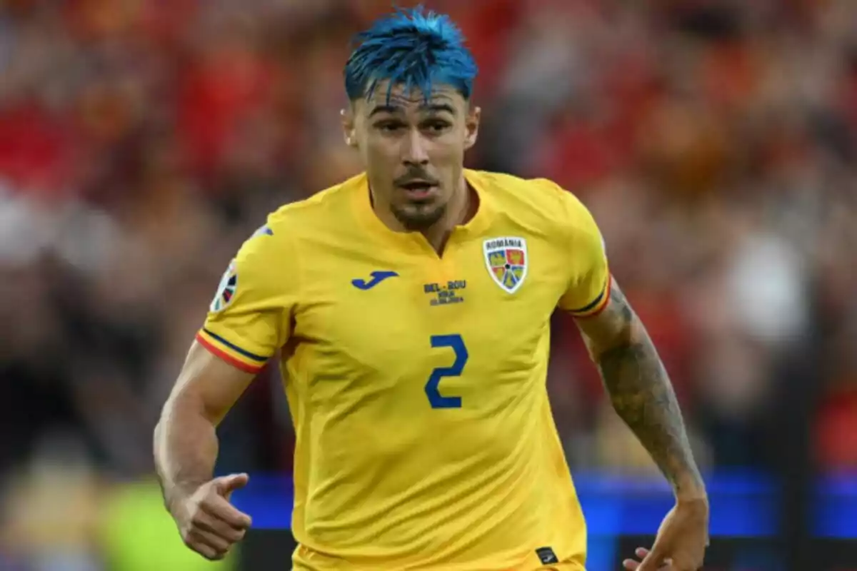 Jugador de fútbol con cabello azul y camiseta amarilla de la selección de Rumania en el campo de juego.