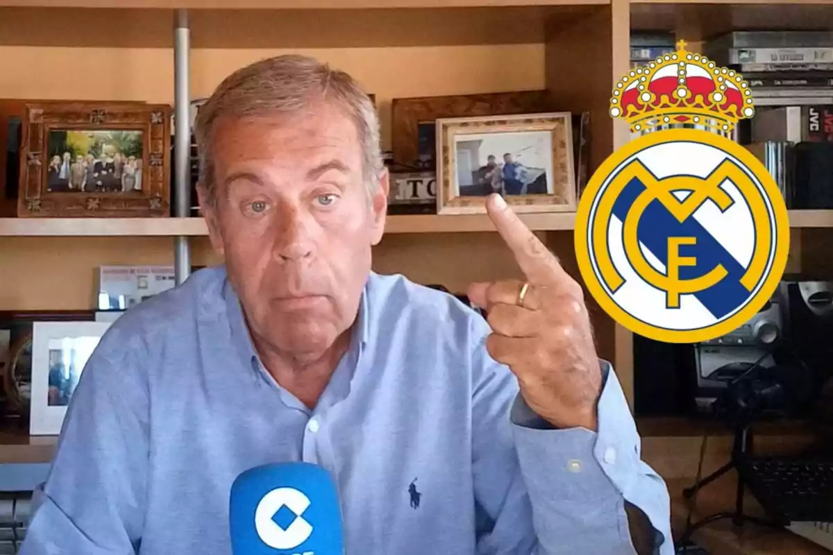 Hombre con camisa azul frente a un micrófono azul, señalando hacia un escudo del Real Madrid en un entorno de oficina con estanterías y fotos enmarcadas.