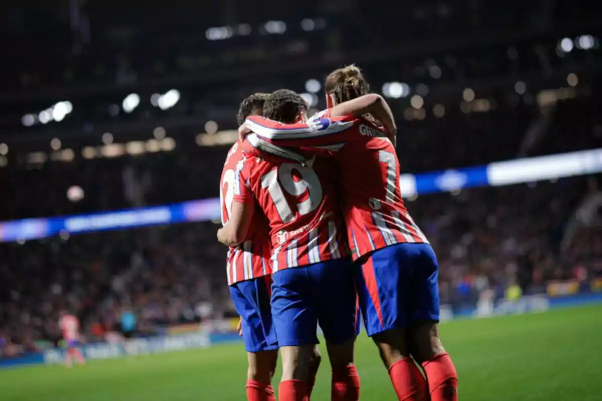 Jugadores de fútbol con uniformes rojos y blancos celebran en el campo abrazados.