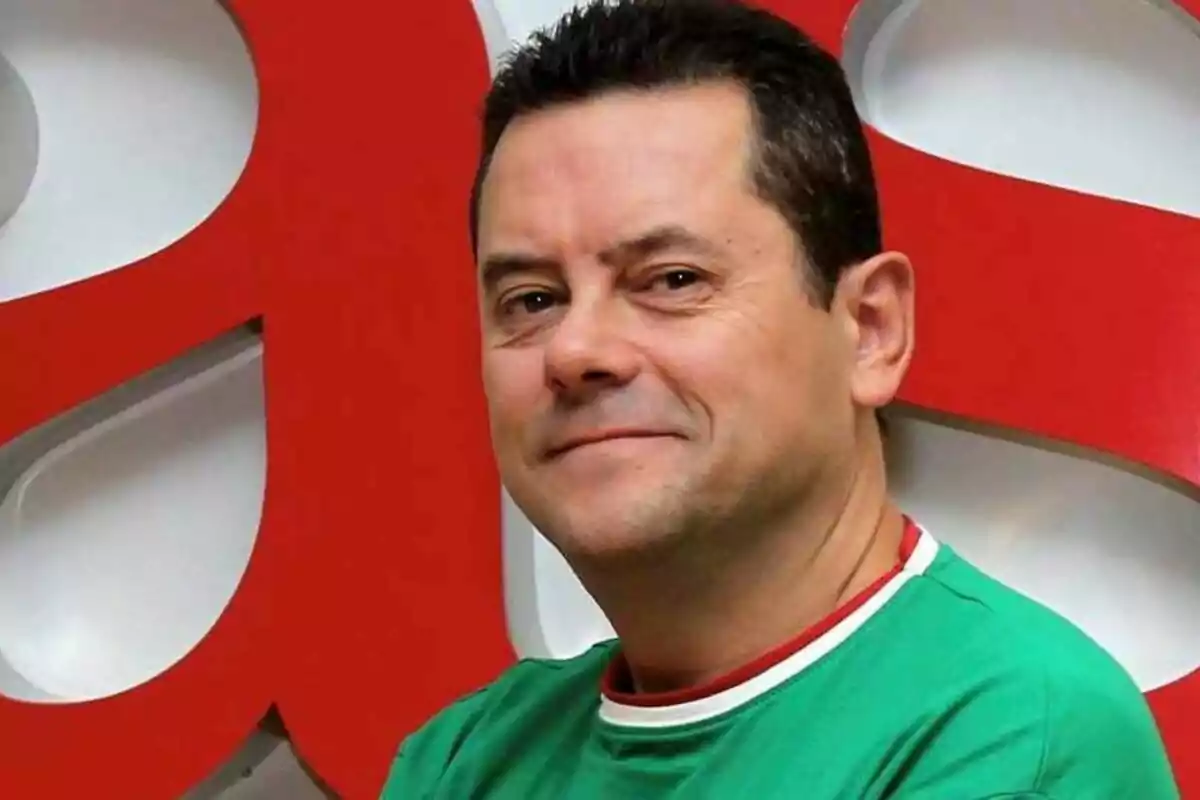 Hombre con camiseta verde sonriendo frente a un fondo rojo y blanco.