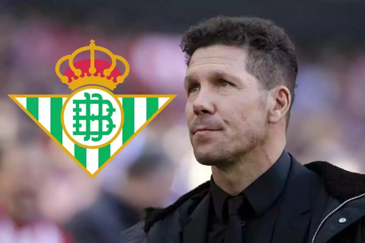 Un hombre con traje oscuro y el logo del Real Betis en el fondo.