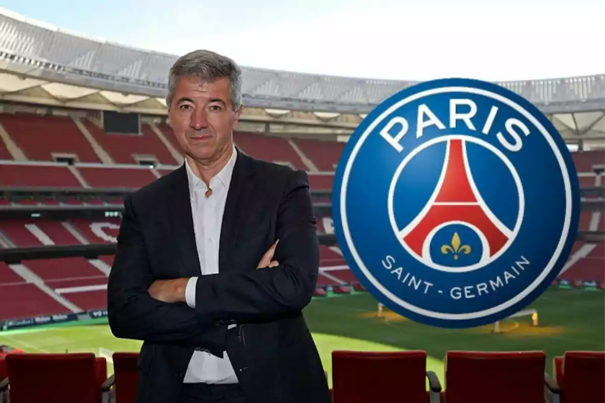 Hombre de traje con los brazos cruzados en un estadio de fútbol con el logo del Paris Saint-Germain al lado.