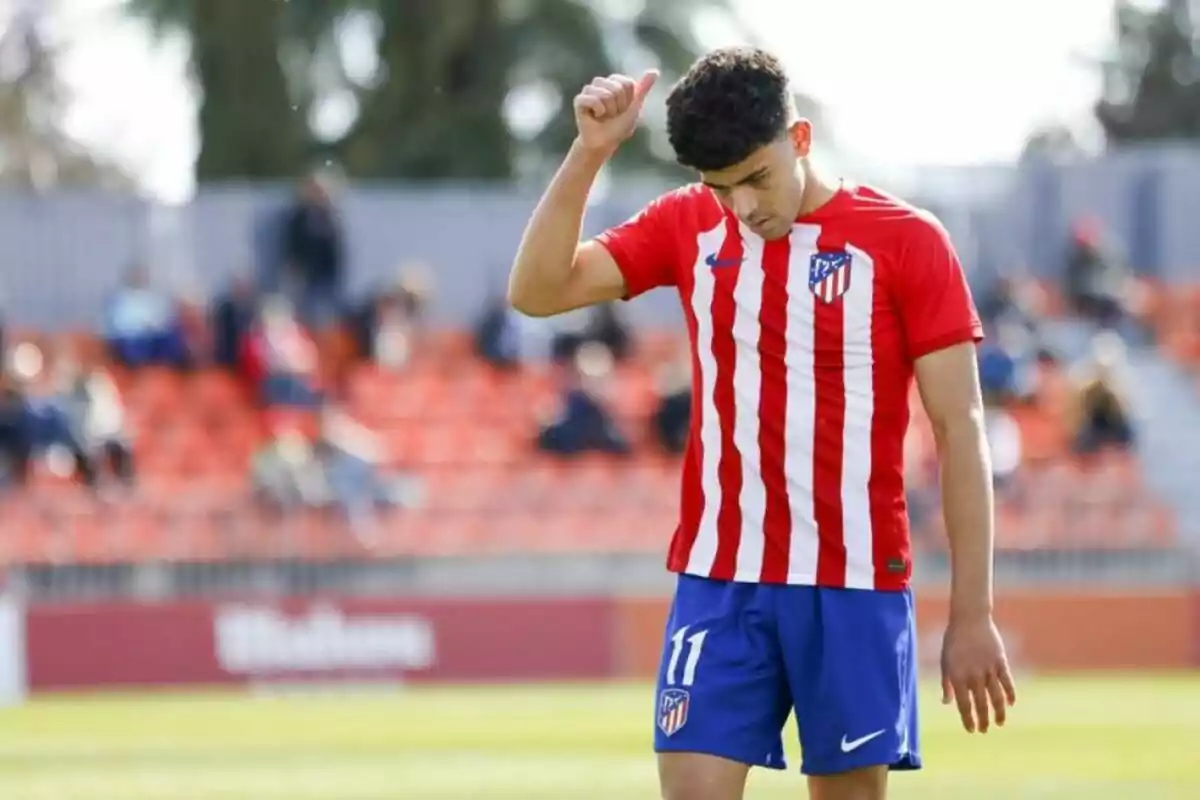 Football player in Atletico Madrid uniform giving thumbs up on a playing field.