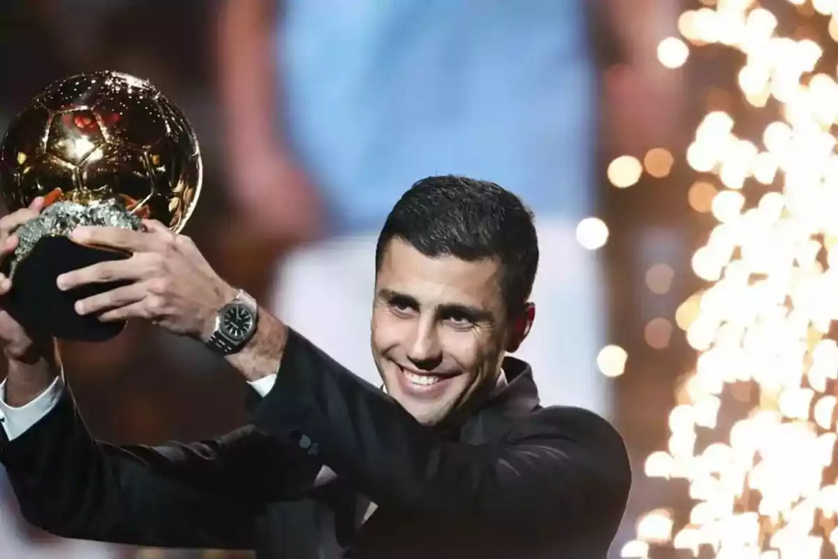 Person holding a golden trophy with a happy expression and bright lights in the background.